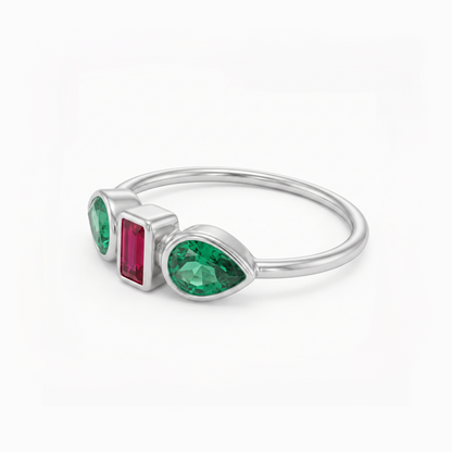 A silver ring featuring three gemstones: a large pear-cut green emerald, a rectangular pink ruby emerald, and a smaller pear-cut green emerald, set in a polished silver band on a white background.