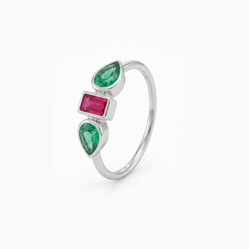A silver ring featuring three vertically aligned gemstones: two pear-cut emerald-cut green stones and one rectangular emerald-cut pink stone, set in a polished silver band against a clean white background.
