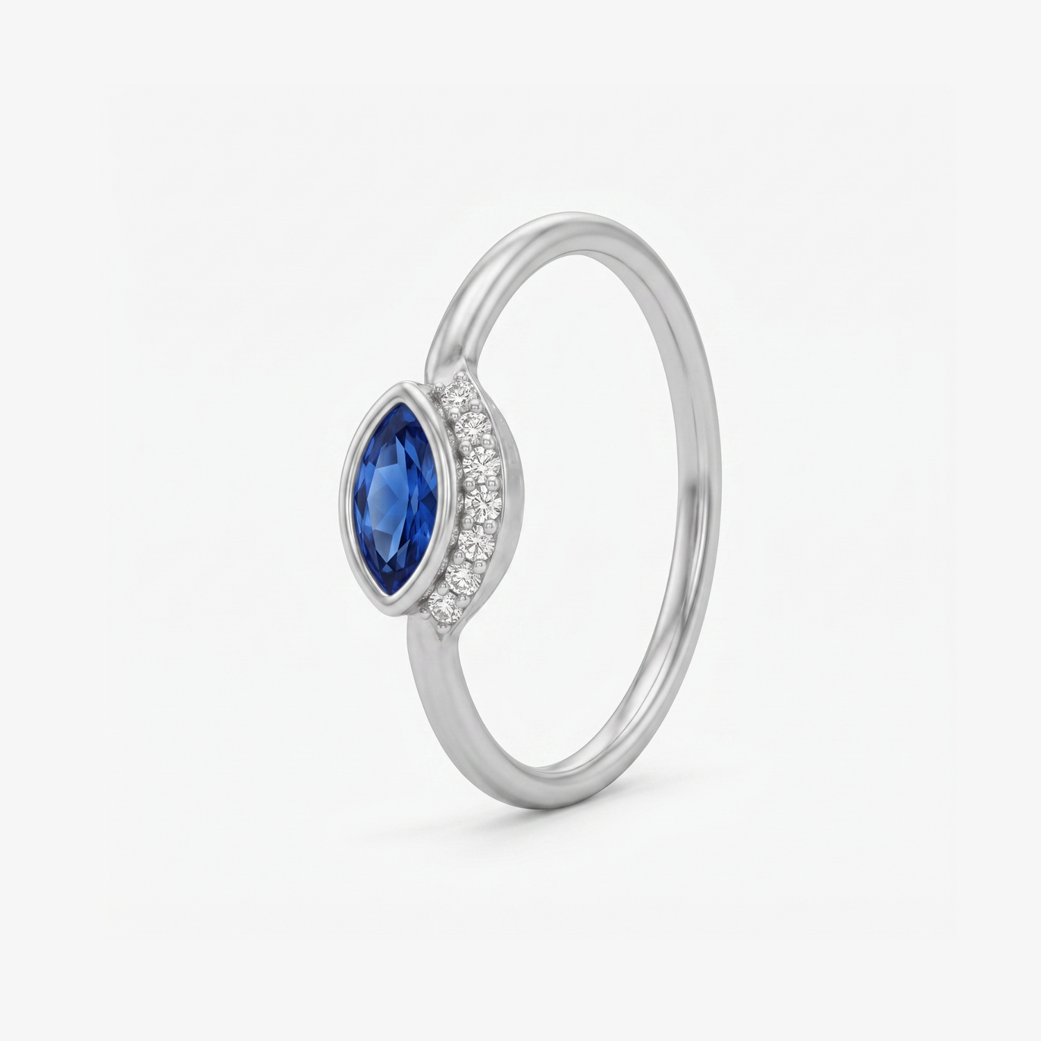 A silver ring featuring a marquise-cut blue sapphire center stone and a halo of small clear stones on the band, shown on a light gray background.