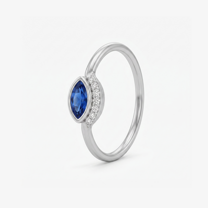 A silver ring featuring a marquise-cut blue sapphire center stone and a halo of small clear stones on the band, shown on a light gray background.