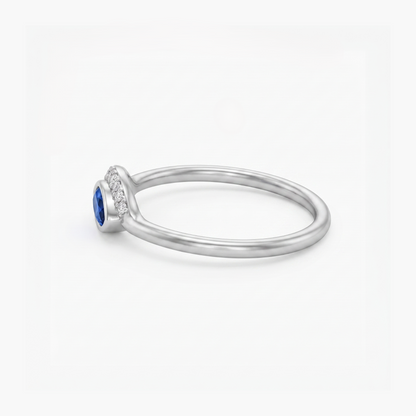 A silver ring featuring a round-cut blue sapphire center stone and a halo of small clear stones along the shank, shown on a clean white background.