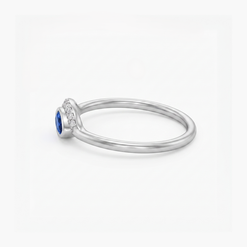 A silver ring featuring a round-cut blue sapphire center stone and a halo of small clear stones along the shank, shown on a clean white background.