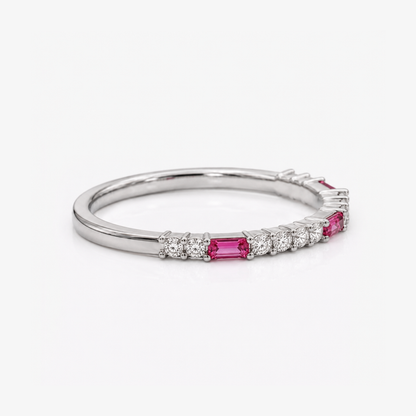 A silver band ring featuring a row of baguette-cut pink gemstones and small round clear stones, photographed on a clean white background.