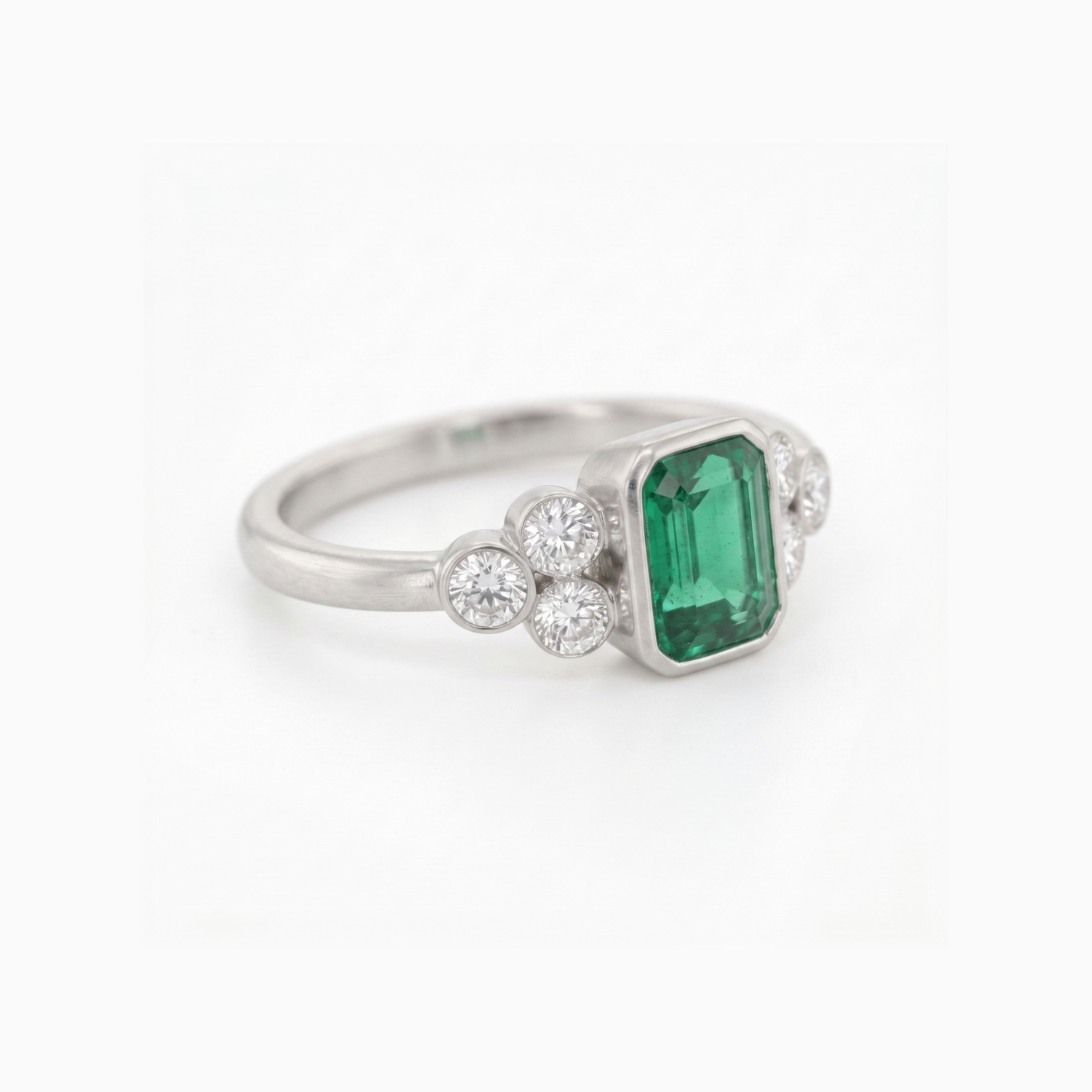 A silver ring featuring a rectangular emerald-cut green gemstone center, flanked by small round clear stones on each side, set against a plain white background.
