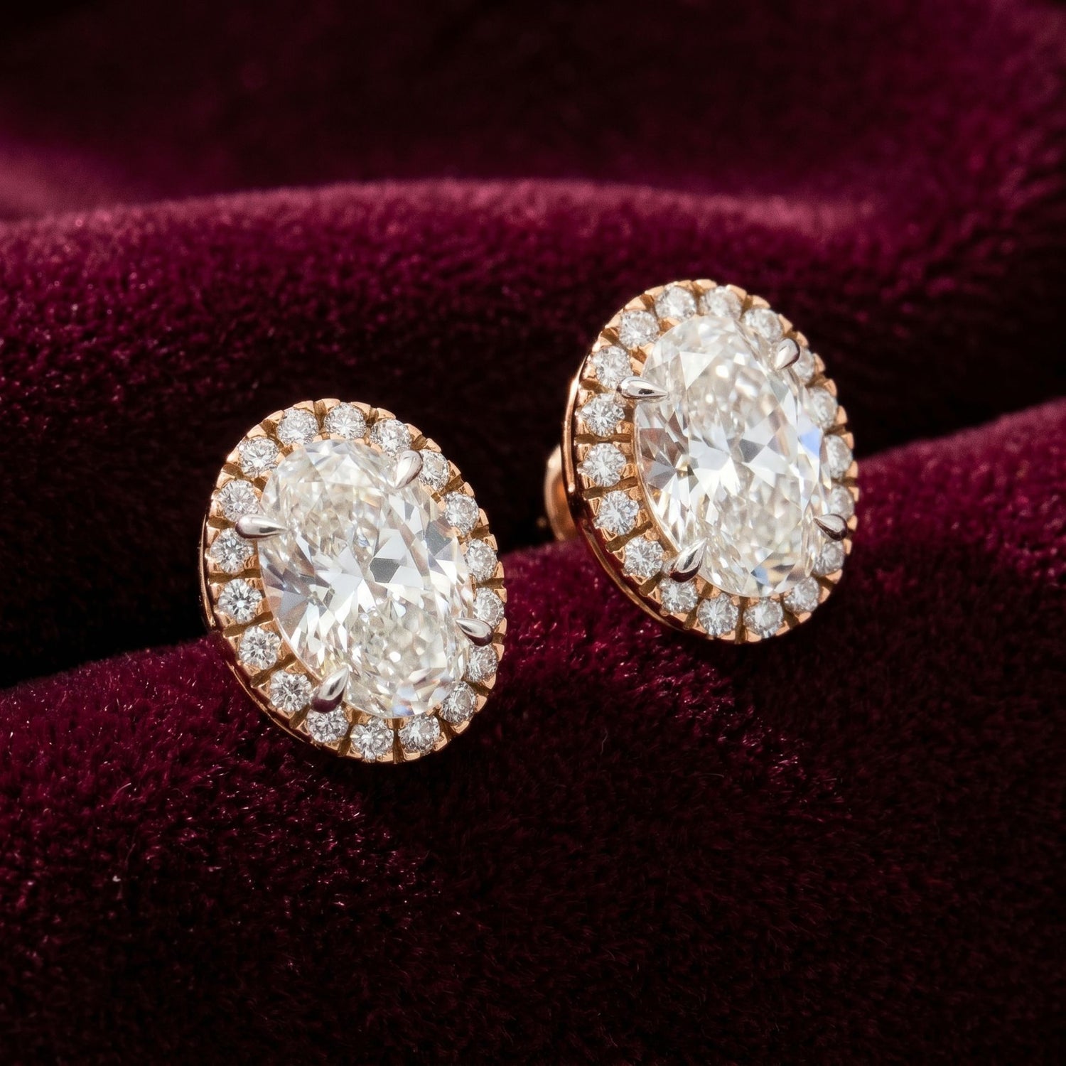 Oval halo lab grown diamond stud earrings on a burgundy velvet background