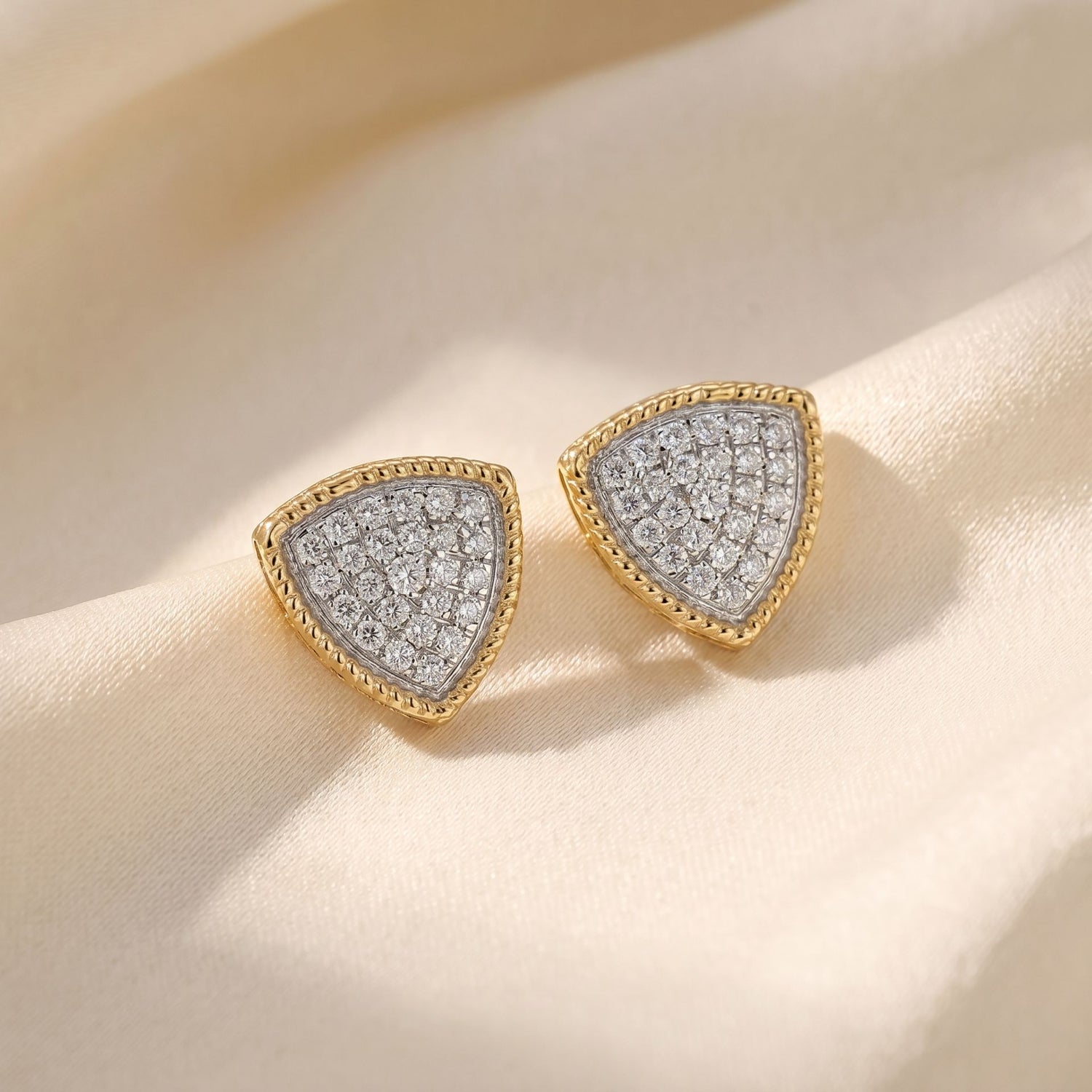Gold triangle lab grown diamond stud earrings on a beige satin background