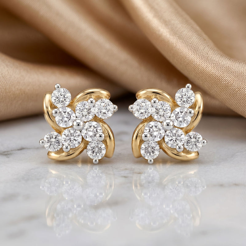 Gold earrings with diamond flowers on a marble surface with beige fabric background