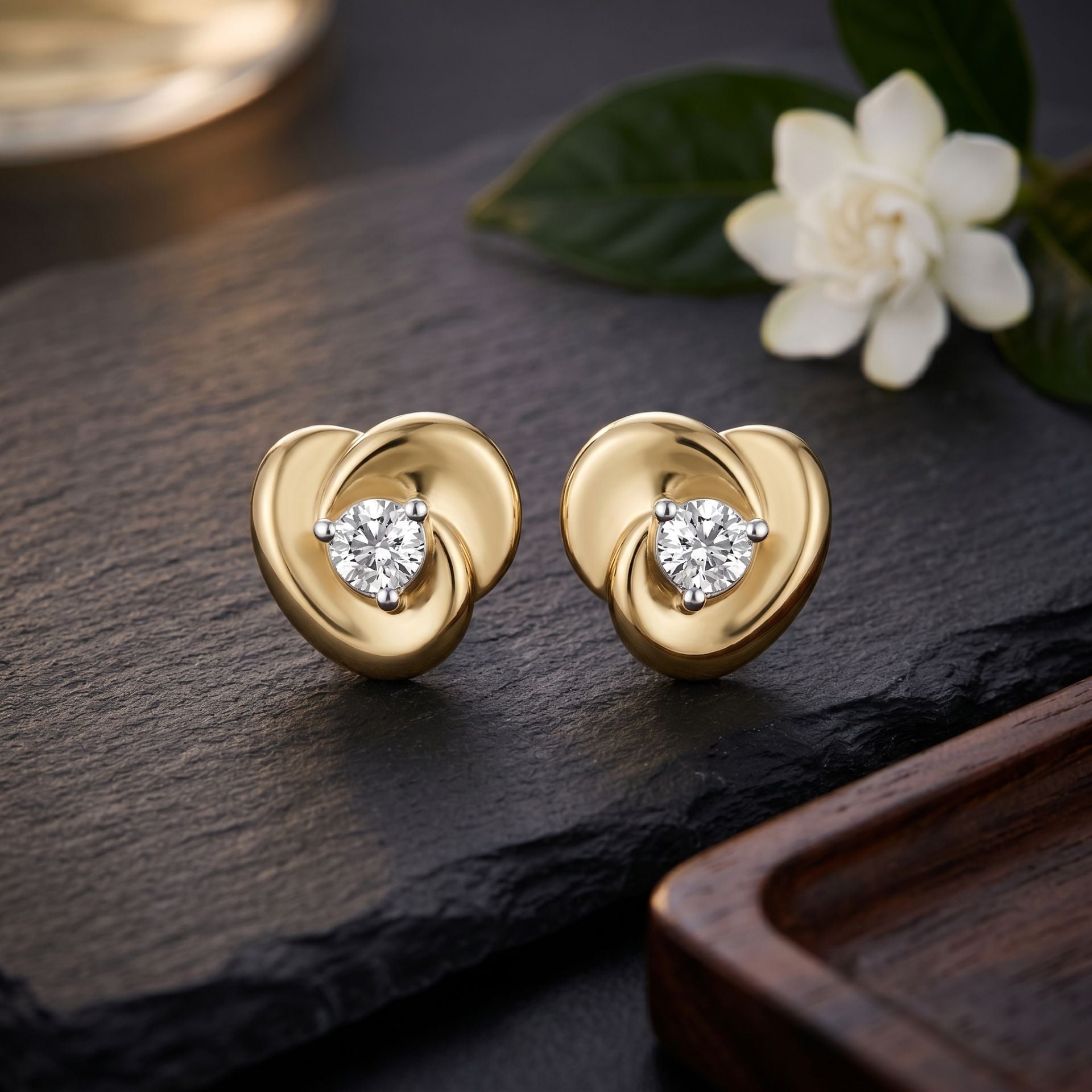 Gold heart-shaped earrings with diamond accents on a dark surface with a flower.