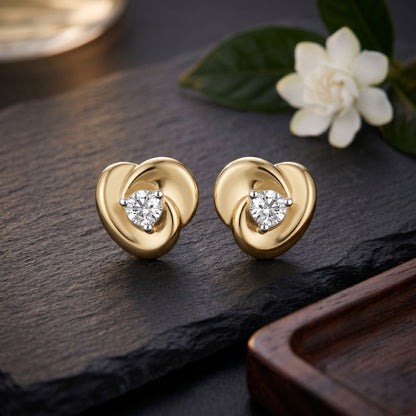 Gold heart-shaped earrings with diamond accents on a dark surface with a flower.
