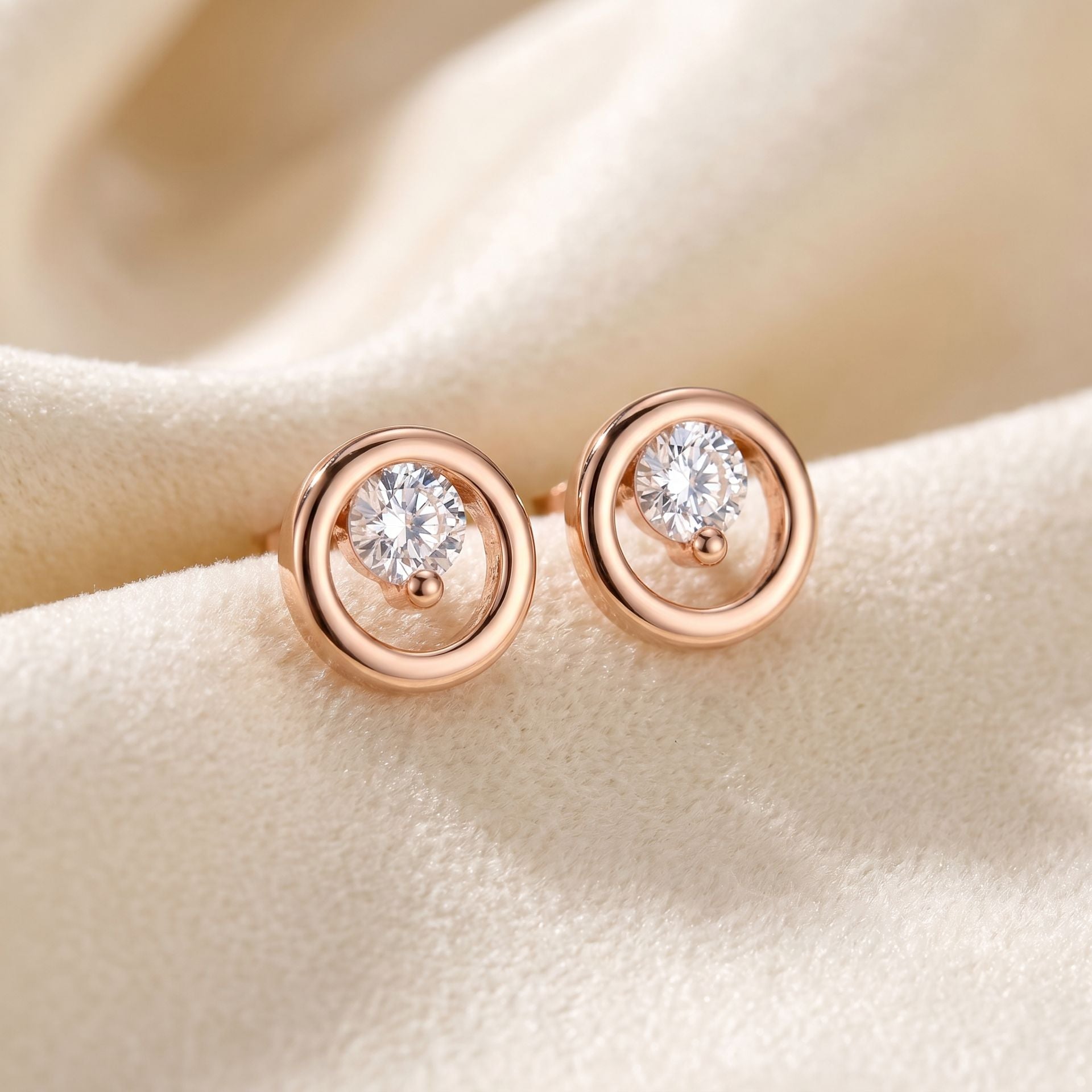 Rose gold earrings with clear gemstones on a beige fabric background